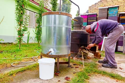 Man is throwing firewood for maintaining fire under the distillation apparatu Stock Photos