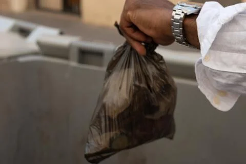 Man throwing garbage bag into dumpster outside Stock-Fotos