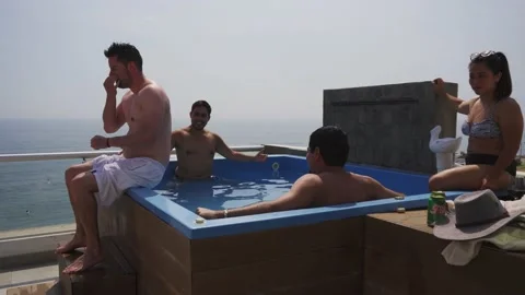 A man throwing himself on his back in a pool with several friends drinking 库存影片 189094466