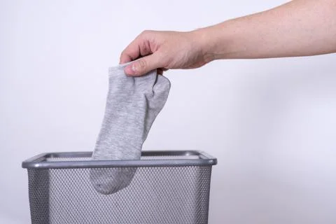 Man throwing an old sock with his hand into a trash can against a gray backgr Foto stock