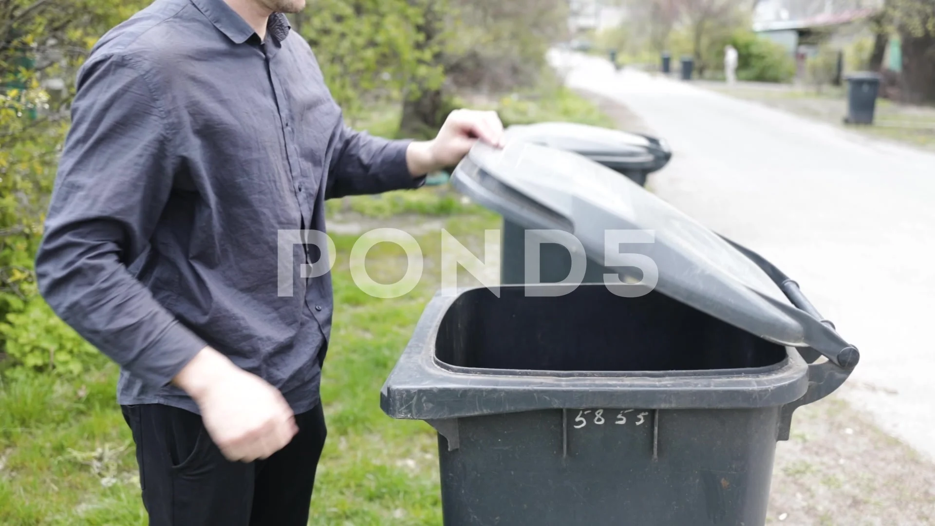 Man throwing out black eco-friendly recyclable trash bag in to big plastic  green garbage container. Stock Photo by nikolast1