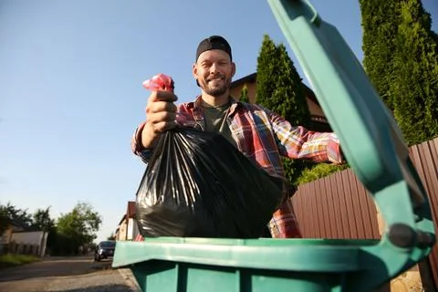 Man throwing trash bag full of garbage into bin outdoors, low angle view. S.. Stock Photos