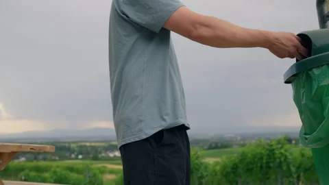 Man Throwing Trash Into Bin Outdoors in Scenic Landscape 库存影片 339034048
