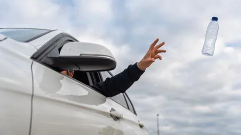 Man throwing a used plastic bottle of water out of his car and polluting the Stock Photos