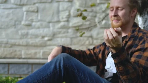 A man throws up and bites an apple while sitting in the garden Stock Footage 200826199