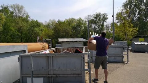 Man throws cardboard box of garbage into containers at large-size waste station Foto stock