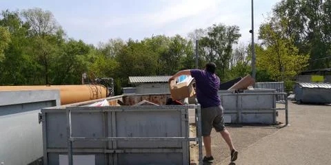 Man throws cardboard box of garbage into containers at large-size waste station Stock Photos