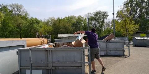 Man throws cardboard box of garbage into containers at large-size waste station Stock Photos