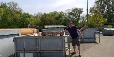 Man throws cardboard box of garbage into containers at large-size waste station Stock Photos