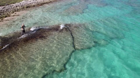 Man throws fishing line standing on stone surrounded by turquoise waters Stock Footage 265834341