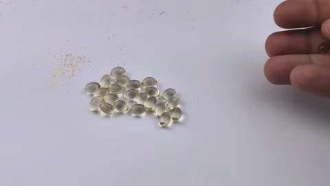 A man throws a handful of Vitamin D3 gelatin tablets on the table. Capsules isol Stock Footage 128530044
