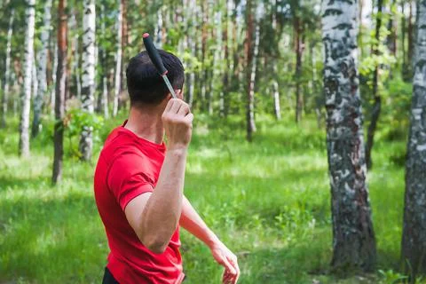 A man throws a knife at a target in the summer forest, back view. Throwing a Stock Photos