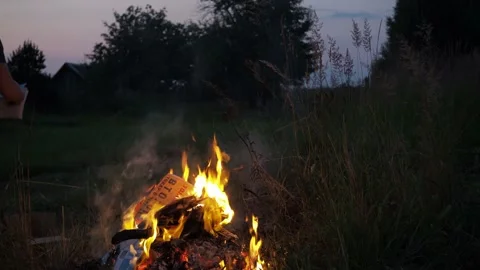 A man throws newspapers in the fire. books, old clothes, tree branches Stock Footage 167694022