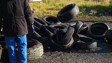 Man throws old tires in a pile from a truck while cleaning area on a spring day Stockbeeldmateriaal 232802417