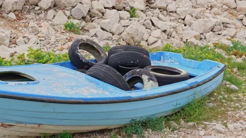A man throws old worn-out car tires into a leaky blue fishing boat. Human waste Stock Footage 219229773