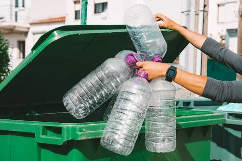 Man throws out empty used big plastic water bottles in to main garbage container Stock Photos