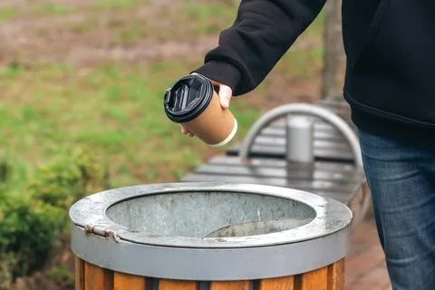 A man throws a paper disposable cup into the trash can in the park. Stock Photos