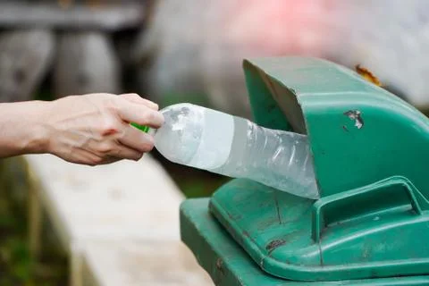 Man throws a plastic water bottle into a green trash bin. Stock Photos