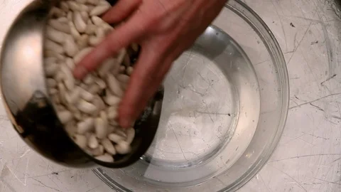 Man throws raw white beans in bowl with water. Top view. Stock Footage 98016381