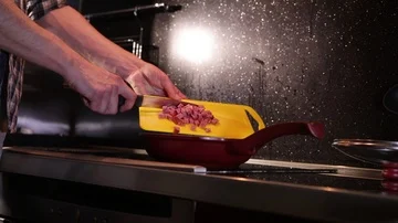 A man throws sausage from a cutting board into a frying pan Stock Footage 86156844