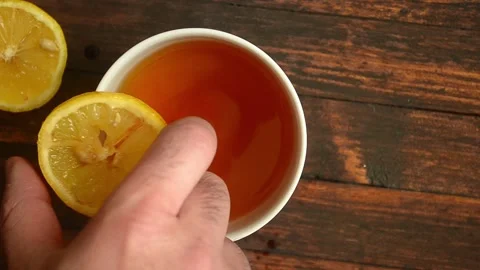 Man throws a slice of lemon into a cup of tea on wooden background Video stock 155177596