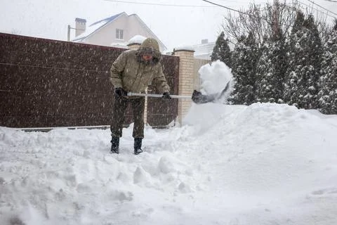 Man throws snow from the front yard of his own house with a plastic shovel 库存照片