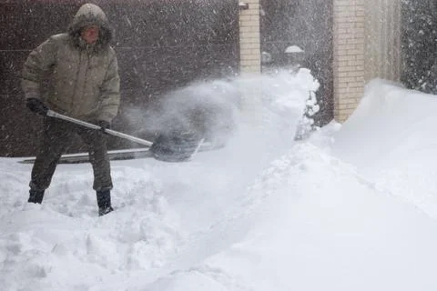 Man throws snow from the front yard of his own house with a plastic shovel 스톡 사진