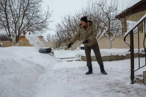 Man throws snow from the front yard of his own house with a plastic shovel 스톡 사진