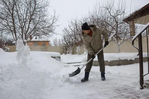 Man throws snow from the front yard of his own house with a plastic shovel Stock-Fotos