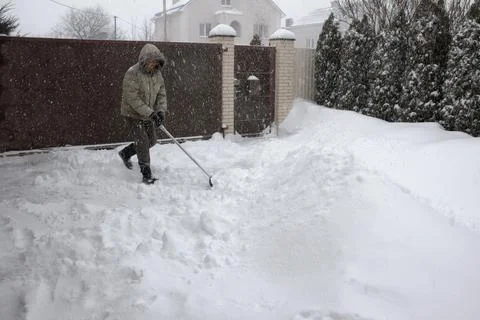 Man throws snow from the front yard of his own house with a plastic shovel 스톡 사진