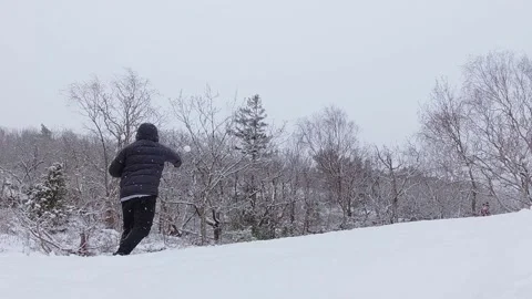 A man throws a snowball against a tree while snow is falling Stock Footage 146901836