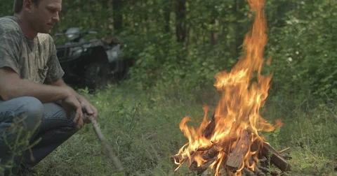 Man throws stick into campfire in the forest Stock Footage 76703247