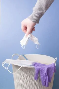 A man throws a used protective face mask of blue color into a trash can, blue Stock Photos
