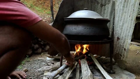 Man throws wood to boiling pot while cooking outdoor with open fire Stock Footage 223885335