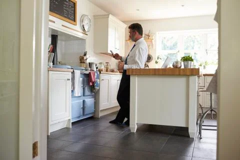 Man in tie standing in kitchen checking his smartphone Stock Photos