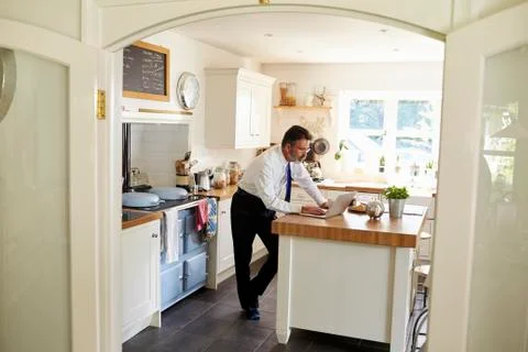 Man in tie using laptop at kitchen island, full length Stock Photos