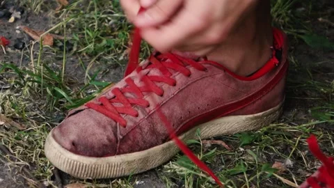 Man ties the laces of old Red sneakers while on the street Stock Footage 132953177