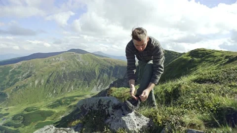 Man ties shoelaces while standing on a stone against the background of mountain Stock Footage 217396929