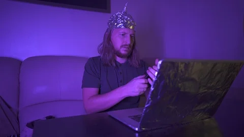 Man in Tin Foil Hat type message on phone, work at laptop. Mind control Stock Footage 122429074
