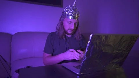 Man in Tin Foil Hat typing message on phone, work at laptop. Global conspiracy Stock Footage 122429073
