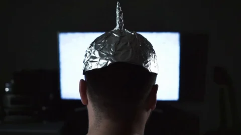 Man in tin foil hat watching white noise on TV screens at home. Stock Footage 128125382