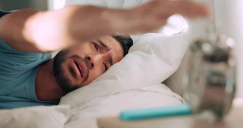 Man tired in bed with alarm time clock to wake up from sleeping in house or home Stock Footage 233990714