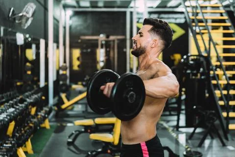 Man with tired expression doing exercises with weight in a gym Stock Photos