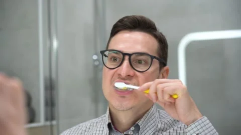 Man with toothbrush cleaning teeth, looking mirror in bathroom close up. Care Stock Footage 131465989