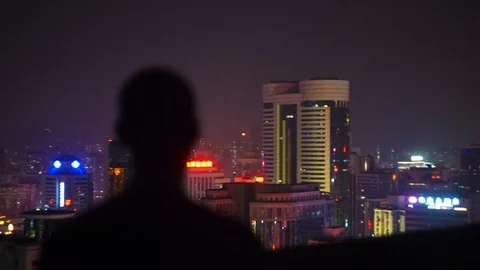 A man on top of a building at night looking to city Stock Footage 76862233