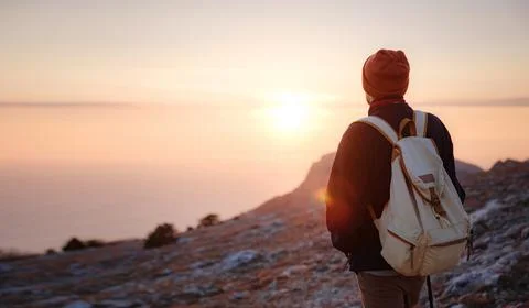 A man on top of a cliff in the spring mountains at sunset and enjoying the vi Stock Photos