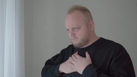 Man Touching Chest and Looking Uncomfortable by Window Stock Footage 343719218