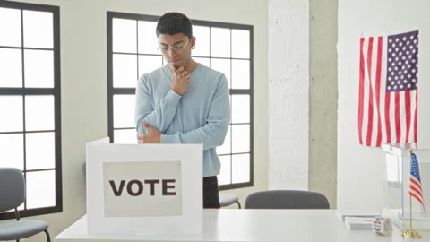 Man touching chin by ballot box in building polling station, wearing glasse.. Stock Footage 337431685