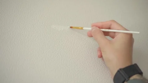 The man is touching up the chips on the wallpaper with a paintbrush. Vídeos de archivo 346546996