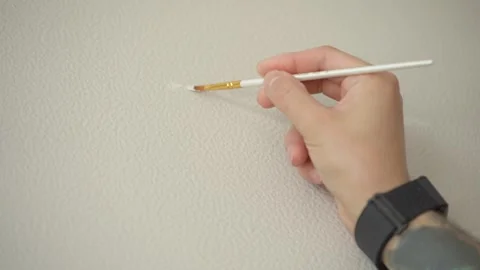 The man is touching up the chips on the wallpaper with a paintbrush. Vídeos de archivo 346547010
